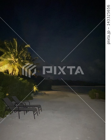 Empty lounge chairs and illuminated palm trees line a tropical beach at night. Empty lounge chairs and illuminated palm trees line a tropical beach at night. 143325656