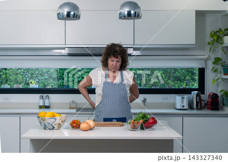 Older Focused cook pausing at her kitchen island amid gathered ingredients 143327340
