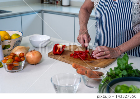 Hands skillfully chopping red peppers on a wooden board in a bright kitchen 143327350