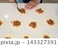 Woman portioning spiced meat filling onto empanada dough rounds with focused efficiency 143327391