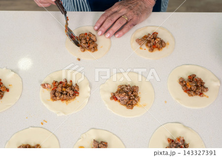 Woman portioning spiced meat filling onto empanada dough rounds with focused efficiency 143327391
