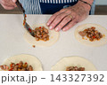 Spooning seasoned ground meat filling onto empanada dough circles with deliberate care 143327392