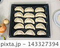 Fifteen unbaked empanadas arranged in neat rows on a dark baking tray ready for the oven 143327394
