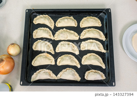 Fifteen unbaked empanadas arranged in neat rows on a dark baking tray ready for the oven 143327394