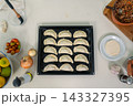 Unbaked empanadas arranged in orderly rows on a dark baking sheet surrounded by fresh ingredients 143327395