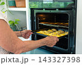 Pulling a tray of golden empanadas from a heated oven with practiced ease 143327398