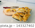 Crispy golden empanadas arranged on a ceramic plate beside a wooden cutting board 143327402