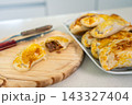 Freshly baked empanadas displayed on a wooden board and white plate in bright kitchen light 143327404