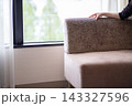 カウチソファの背もたれに手をかける女性の手。窓際の明るい部屋。 143327596