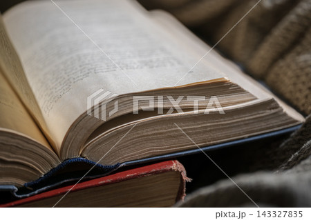 Open old book with weathered pages lying on a rustic knitted blanket representing education and knowledge Open old book with weathered pages lying on a rustic knitted blanket representing education and knowledge 143327835