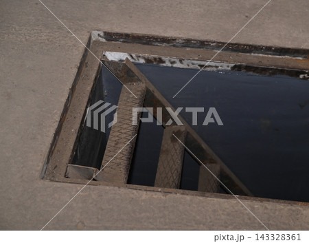 Open hatch leads down via industrial metal stairs into dark basement. 143328361