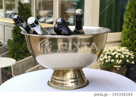 Chilled champagne bottles in an elegant silver ice bucket on an outdoor terrace, creating a luxurious setting for celebration, hospitality, and special occasions. Chilled champagne bottles in an elegant silver ice bucket on an outdoor terrace, creating a luxurious setting for celebration, hospitality, and special occasions. 143330193