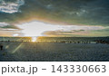 雲の切れ間から夕光が差し込む海岸と佇む人々 白い石浜の夕景写真素材 143330663