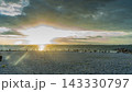 雲の切れ間から夕光が差し込む海岸と佇む人々 白い石浜の夕景写真素材 143330797