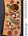 Snacks and sandwiches with dried tomatoes on wooden board. 143330943