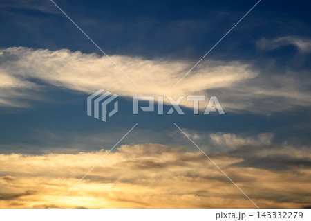 long golden cloud in a blue sky illuminated by the setting sun long golden cloud in a blue sky illuminated by the setting sun 143332279