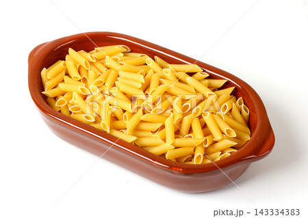Uncooked penne pasta in a brown ceramic bowl isolated on a white background. Uncooked penne pasta in a brown ceramic bowl isolated on a white background. 143334383