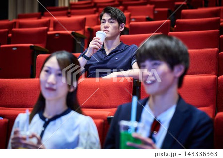 映画館でドリンクを飲みながら真剣に映画を鑑賞する男性 映画館でドリンクを飲みながら真剣に映画を鑑賞する男性 143336363