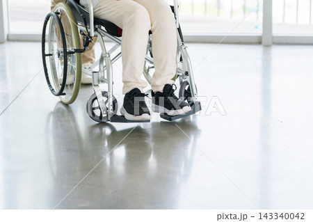 車椅子に乗るシニア女性と介護施設で働く女性スタッフ 車椅子に乗るシニア女性と介護施設で働く女性スタッフ 143340042