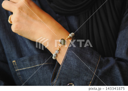 A woman shows a bracelet on their wrist while wearing a denim shirt A woman shows a bracelet on their wrist while wearing a denim shirt 143341875