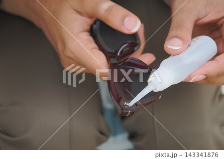 Man applies glue to sunglasses for repair while sitting outdoors Man applies glue to sunglasses for repair while sitting outdoors 143341876