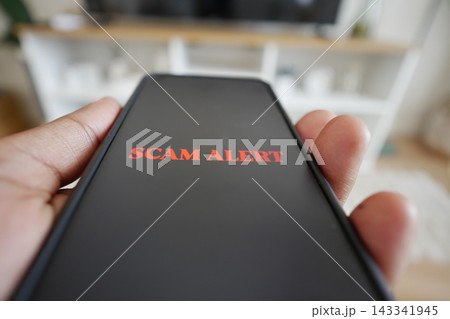 Person holds phone displaying scam alert in home setting 143341945