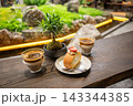 Cozy Cafe Table With Coffee Cups, Strawberry Roll Cake and Bonsai Plant Overlooking Garden 143344385