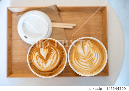 Two Lattes With Latte Art on Wooden Tray in Bright Cafe Setting for Morning Coffee Two Lattes With Latte Art on Wooden Tray in Bright Cafe Setting for Morning Coffee 143344390