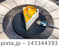 A slice of vibrant yellow and orange cheesecake on a marble table 143344393