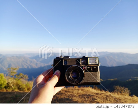 Close up woman hand holding vintage black film camera on the mountain Close up woman hand holding vintage black film camera on the mountain 143347875
