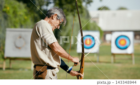 Older man practicing archery aiming for targets 143348944