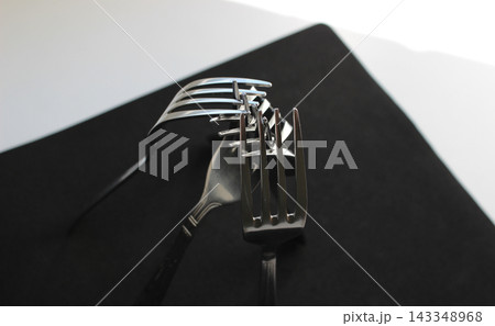 Identical forks from the same kitchen set are arranged in the shape of a tent on black napkin Identical forks from the same kitchen set are arranged in the shape of a tent on black napkin 143348968