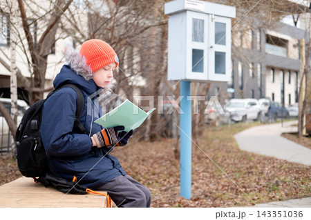 Schoolboy with backpack sitting on bench and reading notebook, repeating lessons before school in autumn park. Schoolboy with backpack sitting on bench and reading notebook, repeating lessons before school in autumn park. 143351036