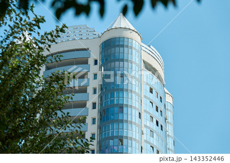 Low angle shot showing top floors and distinctive glass corner turrets of a high-rise white and blue residential building rising against clear blue sky 143352446