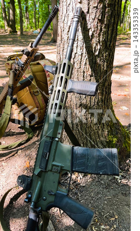 Military Rifle, Assault Rifle and Backpack Standing Near a Tree in a Forest 143353339
