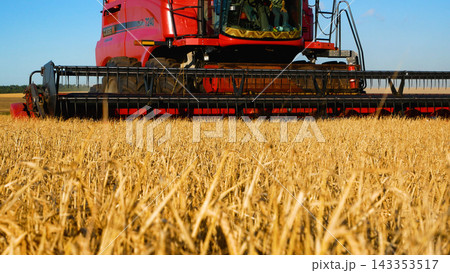 A combine harvester drives through the field, mows ripe wheat and threshes grain. A combine harvester drives through the field, mows ripe wheat and threshes grain. 143353517