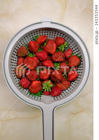 Fresh ripe strawberries in a plastic colander on a marble countertop, top view. Fresh ripe strawberries in a plastic colander on a marble countertop, top view. 143353544