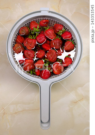 Fresh ripe strawberries in a plastic colander on a marble countertop, top view. 143353545