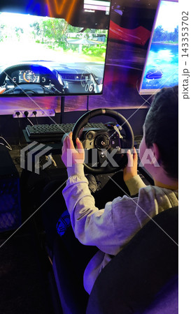 Teenager playing a car driving simulator in an arcade. Teenager playing a car driving simulator in an arcade. 143353702