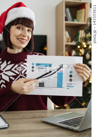 A cheerful individual wearing a Santa hat presents a business report highlighting impressive growth statistics during the holiday season 143355611