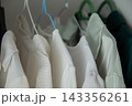 Macro photography of tightly hanging white and mint blouses with embossed small patterns and structural shoulders on multi-colored plastic hangers. Concept: focus on the texture of the material and 143356261