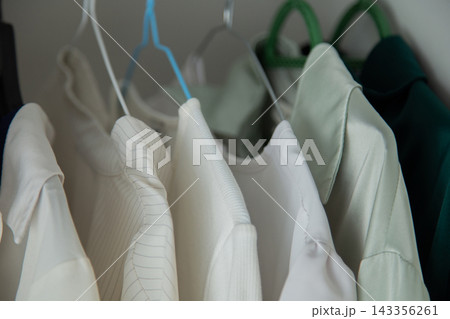 Macro photography of tightly hanging white and mint blouses with embossed small patterns and structural shoulders on multi-colored plastic hangers. Concept: focus on the texture of the material and Macro photography of tightly hanging white and mint blouses with embossed small patterns and structural shoulders on multi-colored plastic hangers. Concept: focus on the texture of the material and 143356261