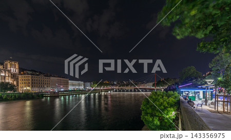 Panorama showing night timelapse of Lyon's cityscape with the red suspension footbridge over the Saone River. France 143356975