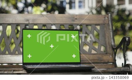 Isolated screen laptop on empty wooden bench outdoors in city park, close up. Replaceable chroma key notebook screen framed by urban greenery and metropolitan buildings Isolated screen laptop on empty wooden bench outdoors in city park, close up. Replaceable chroma key notebook screen framed by urban greenery and metropolitan buildings 143358069