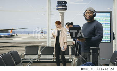 Portrait of casual professional standing in airport terminal with laptop in hand, traveling for global business work via international flight. Black man showcases modern informal culture. 143358178
