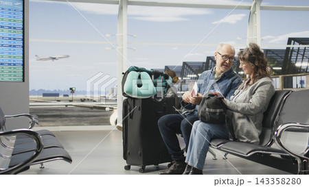 Joyful older adults relaxing in airport terminal engaged in discussion before boarding plane. Mature couple enjoying travel lifestyle, representing active global travel and sightseeing. 143358280