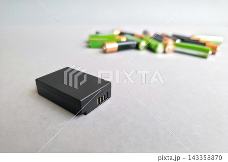 Single rechargeable battery in focus and pile of disposable batteries blurred behind, copy space. Concept of smart choice, reusable power, saving money, waste reduction, eco friendly energy Single rechargeable battery in focus and pile of disposable batteries blurred behind, copy space. Concept of smart choice, reusable power, saving money, waste reduction, eco friendly energy 143358870