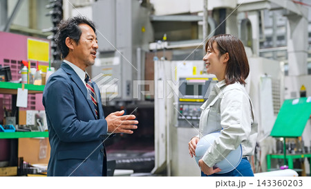 工場で会話する男性ビジネスパーソンと女性作業員 工場で会話する男性ビジネスパーソンと女性作業員 143360203