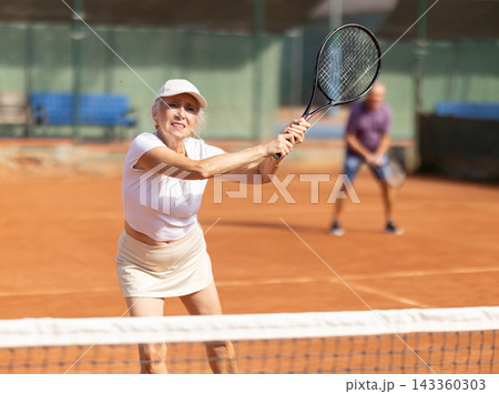 Elderly couple playing tennis together in court Elderly couple playing tennis together in court 143360303