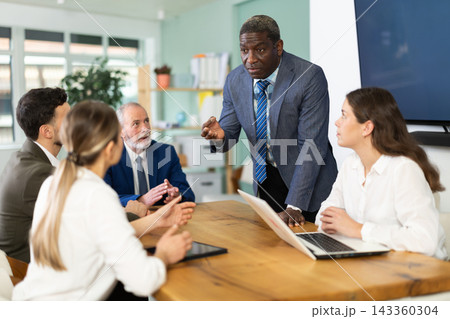 African man stands in front of business colleagues, tells report African man stands in front of business colleagues, tells report 143360304